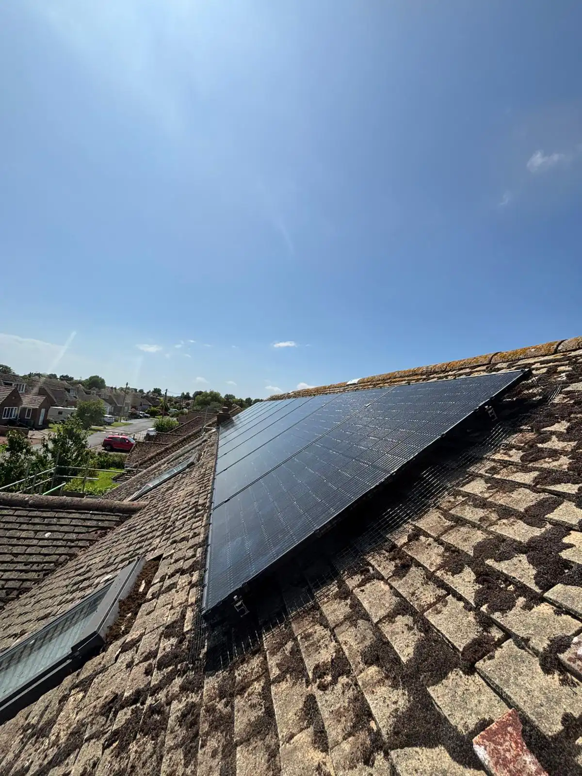 Solar panels installed on a sloped, tiled rooftop under a clear blue sky in a residential neighbourhood.