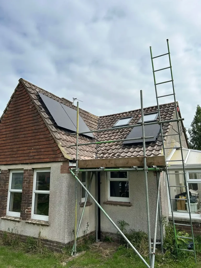 A house with scaffolding and ladders, solar panels installed on the tiled roof under a cloudy sky.