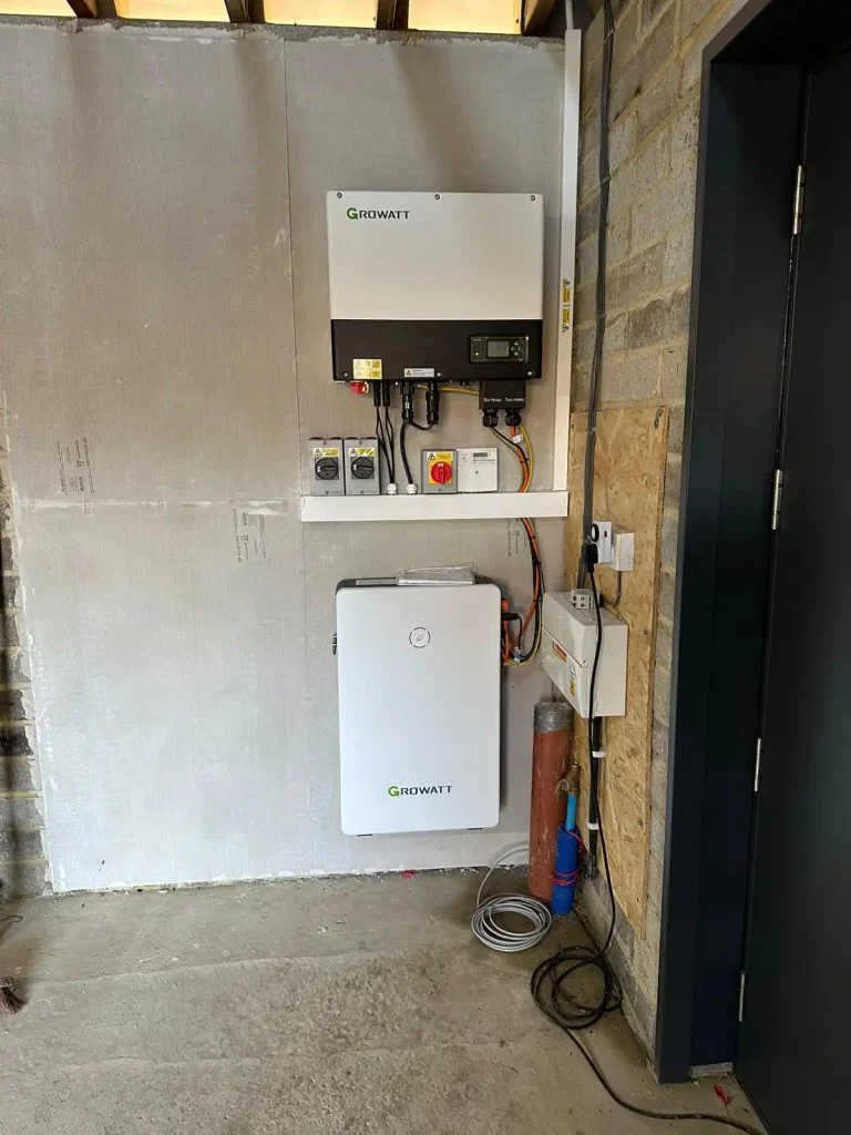 Growatt inverter and battery system mounted on a wall in a utility room with exposed brick and concrete floor.