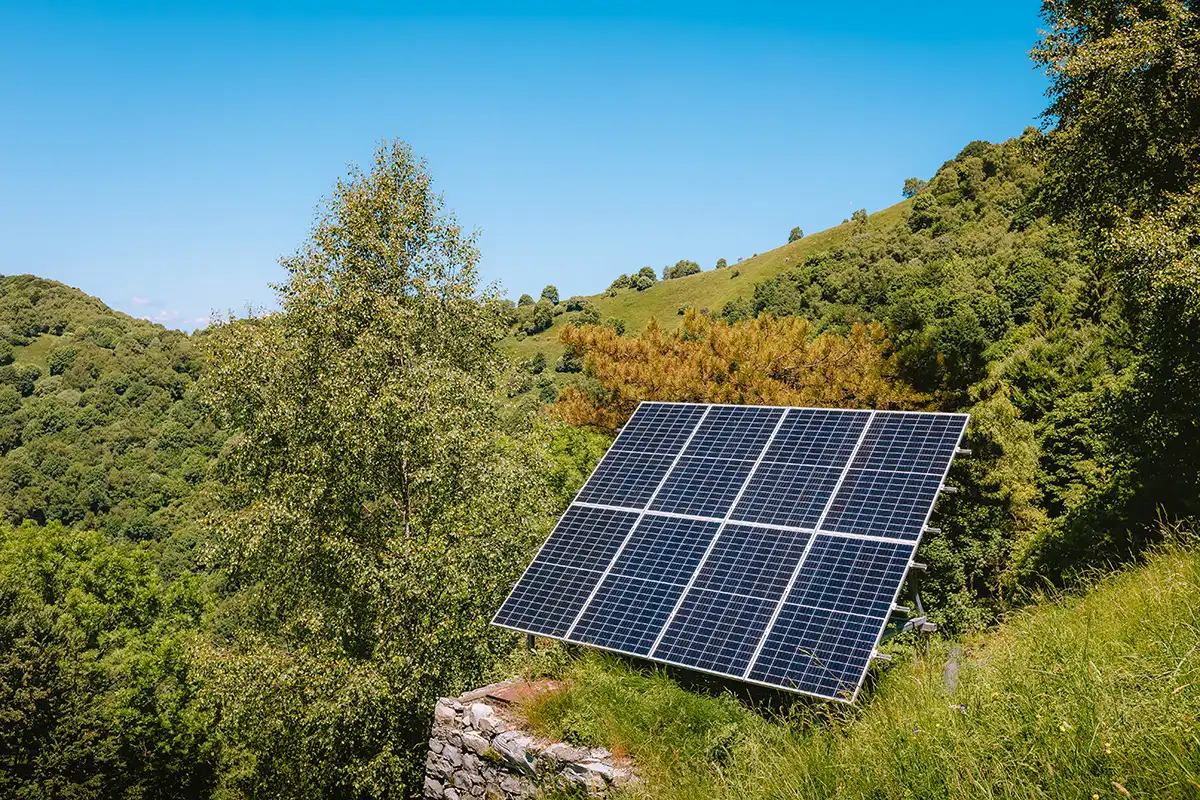 A solar panel in a grassy, hilly landscape surrounded by trees under a clear blue sky.